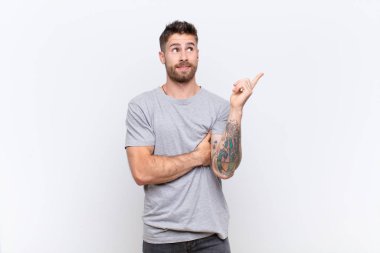 Genç adam mutlu bir şekilde gülümsüyor ve yan bakıyor, merak ediyor, düşünüyor ya da düz renkli duvara karşı bir fikri var.