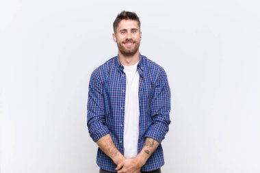 Genç handosme adam pozitif ve kendinden emin gülümsüyor, memnun görünüyor, arkadaş canlısı ve mutlu görünüyor düz renkli duvara karşı