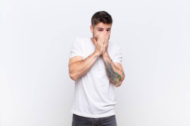 Genç handosme adam endişeli, umutlu ve dindar hissediyor, sadık bir şekilde avuç içleriyle dua ediyor, düz renkli duvara karşı af diliyor.
