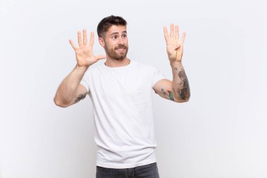 Genç adam gülümsüyor ve dost canlısı görünüyor, dokuzuncu ya da dokuzuncu numarayı gösteriyor, düz renkli duvara doğru sayıyor.