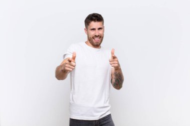 Genç adam kendini mutlu, havalı, tatmin olmuş, rahat ve başarılı hissediyor, kameraya bakıyor, düz renkli duvara karşı seni seçiyor.