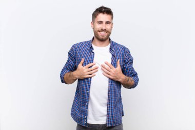 Genç adam mutlu, şaşırmış, gururlu ve heyecanlı görünüyor. Düz renkli duvara işaret ediyor.