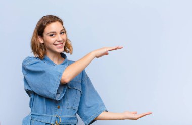 Genç sarışın kadın gülümsüyor, mutlu, pozitif ve tatmin olmuş hissediyor, fotokopi odasında düz renkli duvara karşı nesne ya da konsept tutuyor ya da gösteriyor