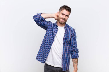 Genç adam neşeli ve kendinden emin bir şekilde gülümsüyor. Düz renkli duvara karşı güler yüzle gülümsüyor.