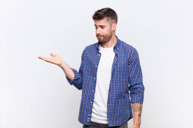 Genç handosme adam mutlu ve gelişigüzel gülümsüyor, düz renkli duvara karşı elde tutulan bir nesneye ya da konsepte bakıyor.