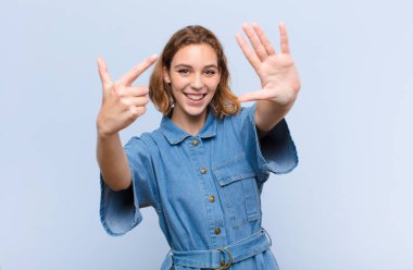 Genç sarışın kadın gülümsüyor ve arkadaş canlısı görünüyor. Yedi ya da yedi numarayı gösteriyor. Elleri önde, düz duvara doğru sayıyor.