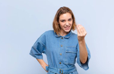 Genç sarışın kadın kapiş ya da para hareketi yapıyor, sana borçlarını ödemeni söylüyor! yassı renk duvarına karşı