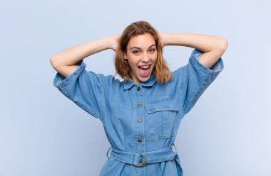 Genç sarışın kadın mutlu, kaygısız, arkadaş canlısı ve rahat görünüyor hayattan ve başarıdan keyif alıyor, düz renkli duvara karşı pozitif bir tutum sergiliyor.