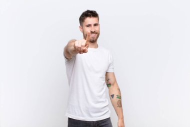 Genç Handosme gururla gülümsüyor ve gururla bir numaralı pozu veriyor. Düz renkli duvara karşı bir lider gibi hissediyor.