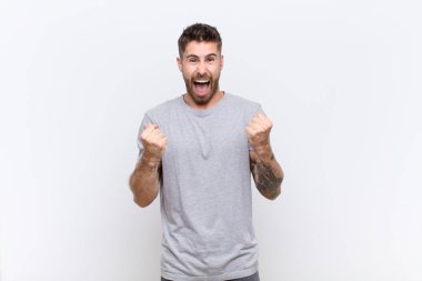 Genç handosme adam sinirli, sinirli, sinirli bir şekilde bağırıyor ve düz renkli duvara karşı öfkeli hissediyor.