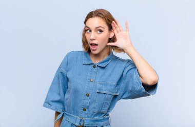 Genç sarışın kadın gülümsüyor, tuhaf bir şekilde yan tarafa bakıyor, dedikoduları dinlemeye çalışıyor ya da düz renkli duvara karşı bir sırrı duymaya çalışıyor.