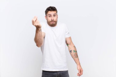 Genç adam kapiş ya da para hareketi yapıyor, sana borçlarını ödemeni söylüyor! yassı renk duvarına karşı