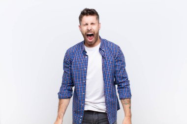 Genç adam agresif bir şekilde bağırıyor, çok kızgın, sinirli, öfkeli ya da sinirli görünüyor, düz renkli duvara karşı hayır diye bağırıyor.