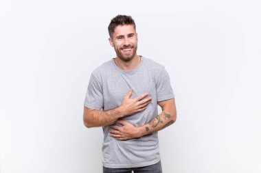 Genç bir adam komik bir şakaya yüksek sesle gülüyor, mutlu ve neşeli hissediyor, düz renkli duvara karşı eğleniyor.