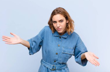 Genç sarışın bir kadın, kafası karışık ve bihaber, hiçbir fikri yok, düz renkli duvara bakan aptal ya da aptal bir bakışla tamamen kafası karışmış.