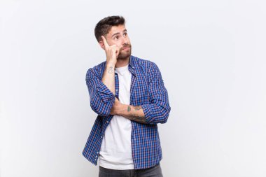 Yoğunlaşmış bakışlı genç bir handosme adam, şüpheli bir ifadeyle merak, düz renk duvar karşı yukarı ve yana bakıyor