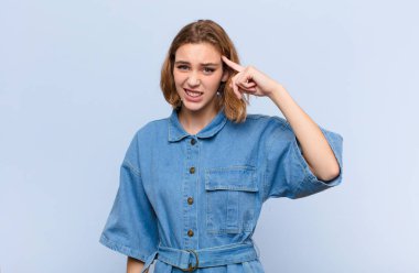 Genç sarışın kadın şaşkın ve şaşkın hissediyor. Deli, deli ya da düz renkli duvara karşı aklını kaçırmış olduğunu gösteriyor.