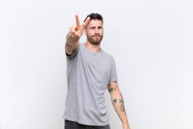 Genç adam gülümsüyor ve mutlu görünüyor, kaygısız ve pozitif, bir eliyle düz bir duvara karşı zafer ya da barış işareti yapıyor.