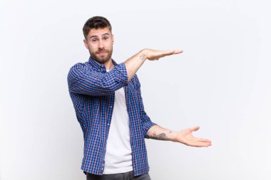 Genç bir handosme adamı iki eliyle bir objeyi tutuyor fotokopi alanında, düz renkli duvara karşı bir nesneyi gösteriyor, sunuyor ya da reklamını yapıyor.