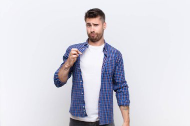 Genç adam kibirli, başarılı, pozitif ve gururlu görünüyor, düz renk duvarına karşı kendini işaret ediyor.