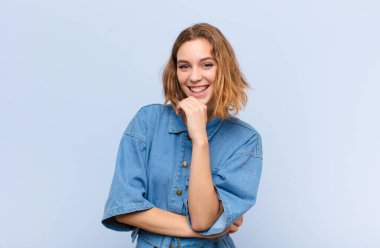 Genç sarışın kadın gülümsüyor, hayattan zevk alıyor, mutlu, arkadaş canlısı, tatmin olmuş ve tasasız.