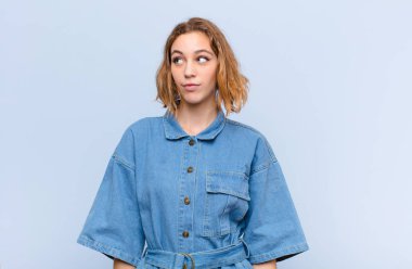 Endişeli, kafası karışık, budala bir ifadeyle genç sarışın kadın kopya alanı arıyor, düz renkli duvara karşı şüpheyle bakıyor.