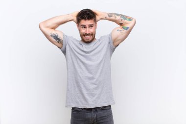 Genç adam kendini stresli, endişeli, endişeli ya da korkmuş hissediyor, elleri başının üstünde, düz renkli duvara karşı panikliyor.