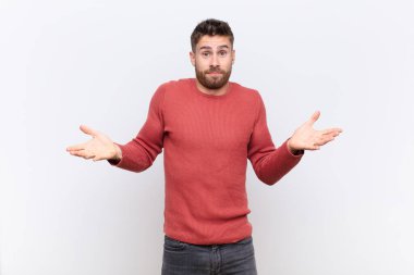 Genç adam şaşkın ve şaşkın hissediyor, doğru cevap ya da karardan emin değil, düz renkli duvara karşı bir seçim yapmaya çalışıyor.