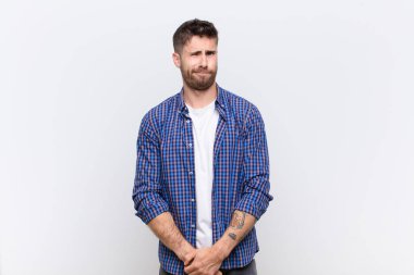 Genç adam mutlu ve arkadaş canlısı görünüyor. Düz renkli duvara karşı olumlu bir tavırla sana gülümsüyor ve göz kırpıyor.