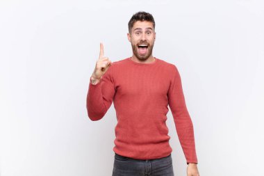 Genç adam bir fikri fark ettikten sonra kendini mutlu ve heyecanlı bir dahi gibi hissediyor. Neşeli bir şekilde parmağını kaldırıyor. Evreka! yassı renk duvarına karşı