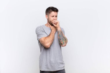 Genç adam boğazı ağrıdığı ve grip belirtileri gösterdiği için hasta. Ağzı düz duvara yapışmış öksürüyor.