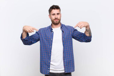 Genç adam gururlu, pozitif ve rahat görünüyor. İki elini de düz duvara dayayıp göğsünü gösteriyor.