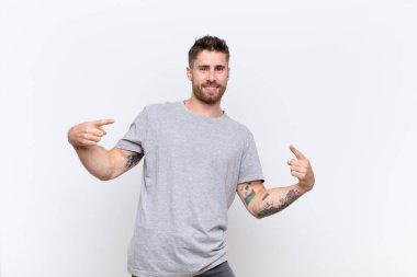 Genç adam gururlu, kibirli, mutlu, şaşırmış ve tatmin olmuş görünüyor, kendini gösteriyor, düz renkli duvara karşı kazanan gibi hissediyor.