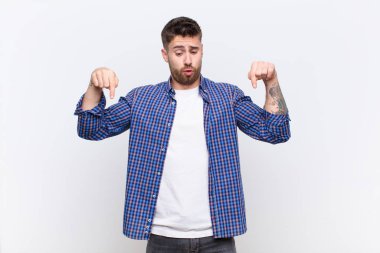 İki eliyle aşağıya doğru bakan ağzı açık genç bir adam, şaşırmış, şaşırmış ve şaşırmış görünüyor.