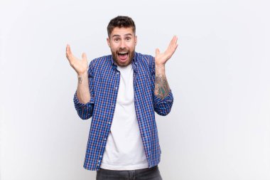 Genç adam şok olmuş ve heyecanlı, gülüyor, şaşırmış ve mutlu çünkü düz renkli duvara karşı beklenmedik bir sürpriz var.