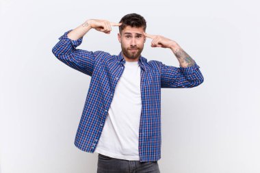 Ciddi ve konsantre görünümlü genç bir handosme adam, düz renk duvarlara karşı zorlu bir sorun düşünüyor ve beyin fırtınası yapıyor.