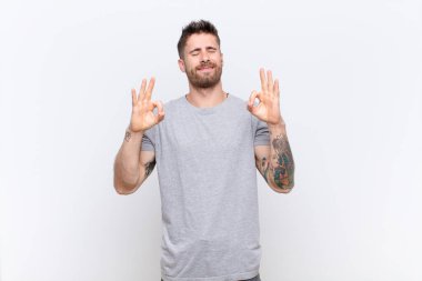 Genç adam konsantre ve meditasyon yapan, kendini tatmin olmuş ve rahat hisseden, düşünen ya da düz renkli duvara karşı seçim yapan biri.