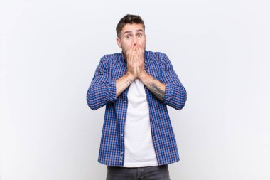 Genç Handome endişeli, üzgün ve korkmuş hissediyor, elleriyle ağzını kapatıyor, endişeli görünüyor ve düz renkli duvara karşı berbat