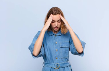 Genç sarışın kadın stresli ve hayal kırıklığına uğramış görünüyor. Baskı altında çalışıyor. Baş ağrısı ve düz renkli duvarlara karşı sorunları var.