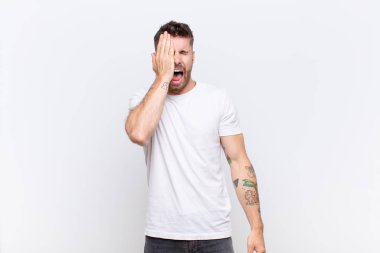 Genç adam uykulu görünüyor, sıkılmış ve esniyor, baş ağrısı ve yüzün yarısını kaplayan düz renkli duvar