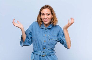 Genç sarışın kadın şaşkın ve şaşkın hissediyor, şüpheci, farklı seçenekleri tartıyor ya da seçiyor düz renkli duvara karşı komik bir ifadeyle