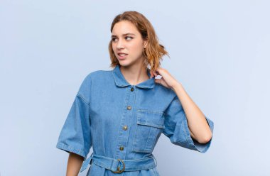 Genç sarışın kadın stresli, endişeli, yorgun ve hayal kırıklığına uğramış, gömleğini çekmiş, düz renkli duvara karşı sorunlu görünüyor.