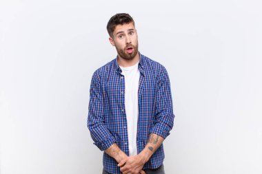 Genç handosme adam şaşkın ve şaşkın hissediyor, aptal, sersemlemiş bir yüz ifadesiyle düz renkli duvara karşı beklenmedik bir şeye bakıyor.