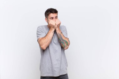 Genç adam endişeli, gergin, stresli ve korkmuş görünüyor, tırnak yiyor ve düz renkli duvara karşı yanal kopyalama alanı arıyor.