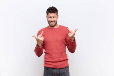 Genç adam kışkırtıcı, agresif ve müstehcen hissediyor, orta parmağı çeviriyor, düz renkli duvara karşı isyankar bir tavır sergiliyor.