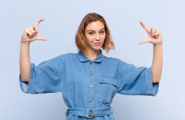 Genç sarışın kadın kendi gülüşünü çiziyor, iki eliyle, pozitif ve mutlu görünüyor, düz renk duvara karşı sağIık kavramı