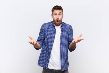 Genç adam ağzı açık ve şaşkın, şaşırmış ve şaşırmış düz renkli duvara karşı inanılmaz bir sürprizle