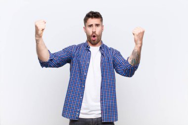 Genç adam inanılmaz bir başarıyı kutluyor. Kazanan gibi. Heyecanlı ve mutlu görünüyor. yassı renk duvarına karşı