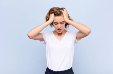 Genç sarışın kadın kendini stresli ve hayal kırıklığına uğramış hissediyor. Yumruk yumruğa, yorgun, mutsuz ve migreni düz renkli duvara dayanmış.