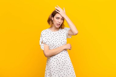 Aptal bir hata yaptıktan ya da hatırladıktan sonra düz bir duvara karşı aptal gibi hisseden genç sarışın bir kadın.